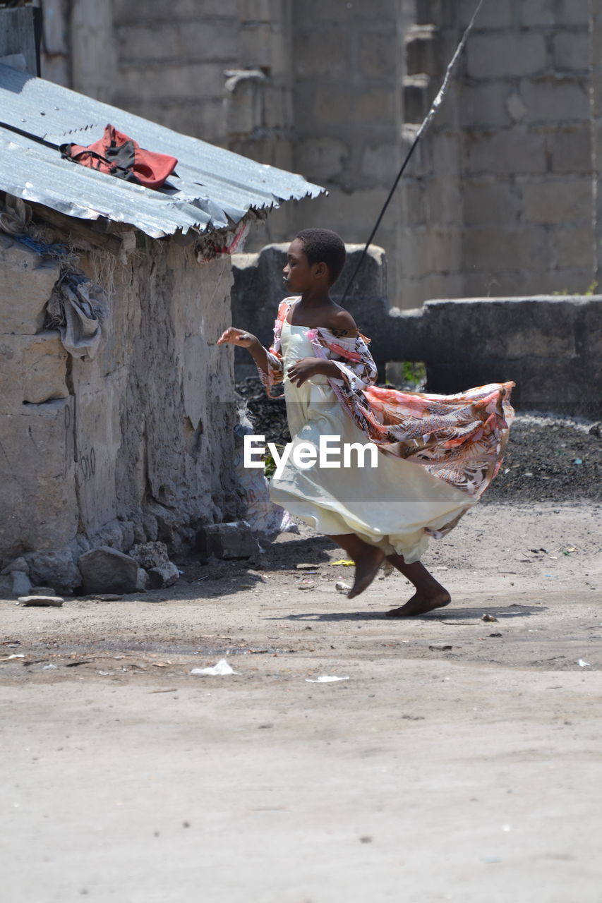 Side view of girl running on road against building during sunny day