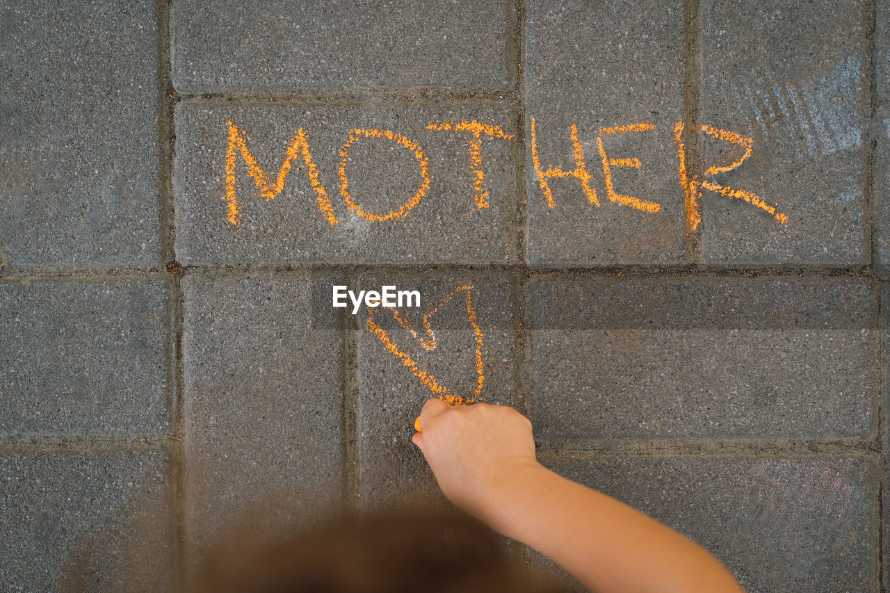Cute boy draws the word mother with chalk. the boy loves his mother.
