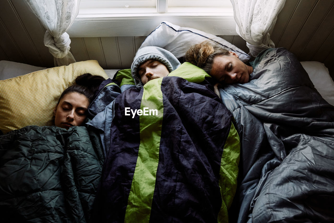 High angle view of male and female friends sleeping together on bed in cottage