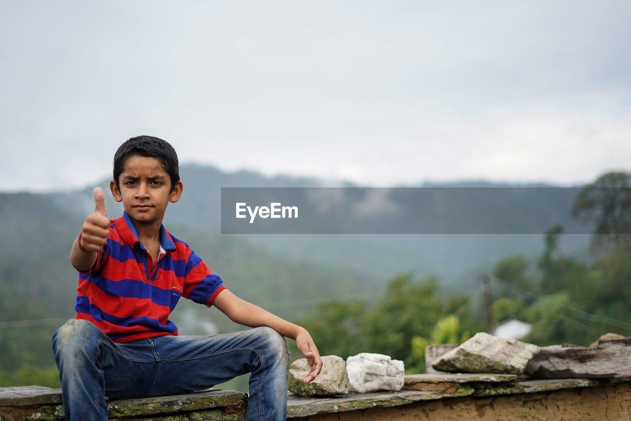 Portrait of a indian pahadi kid who belongs to the mountains showing thumbs up to the camera.
