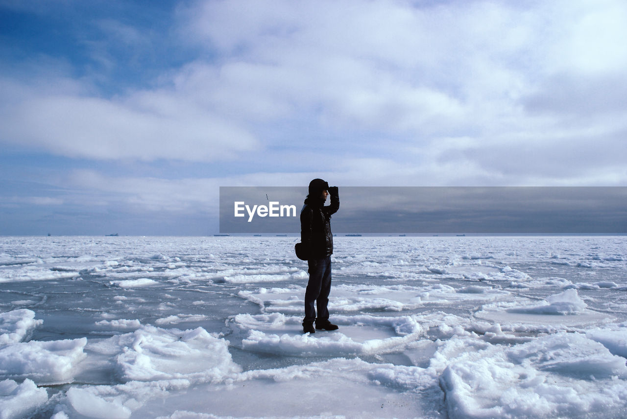 Man standing on snow covered lake against sky