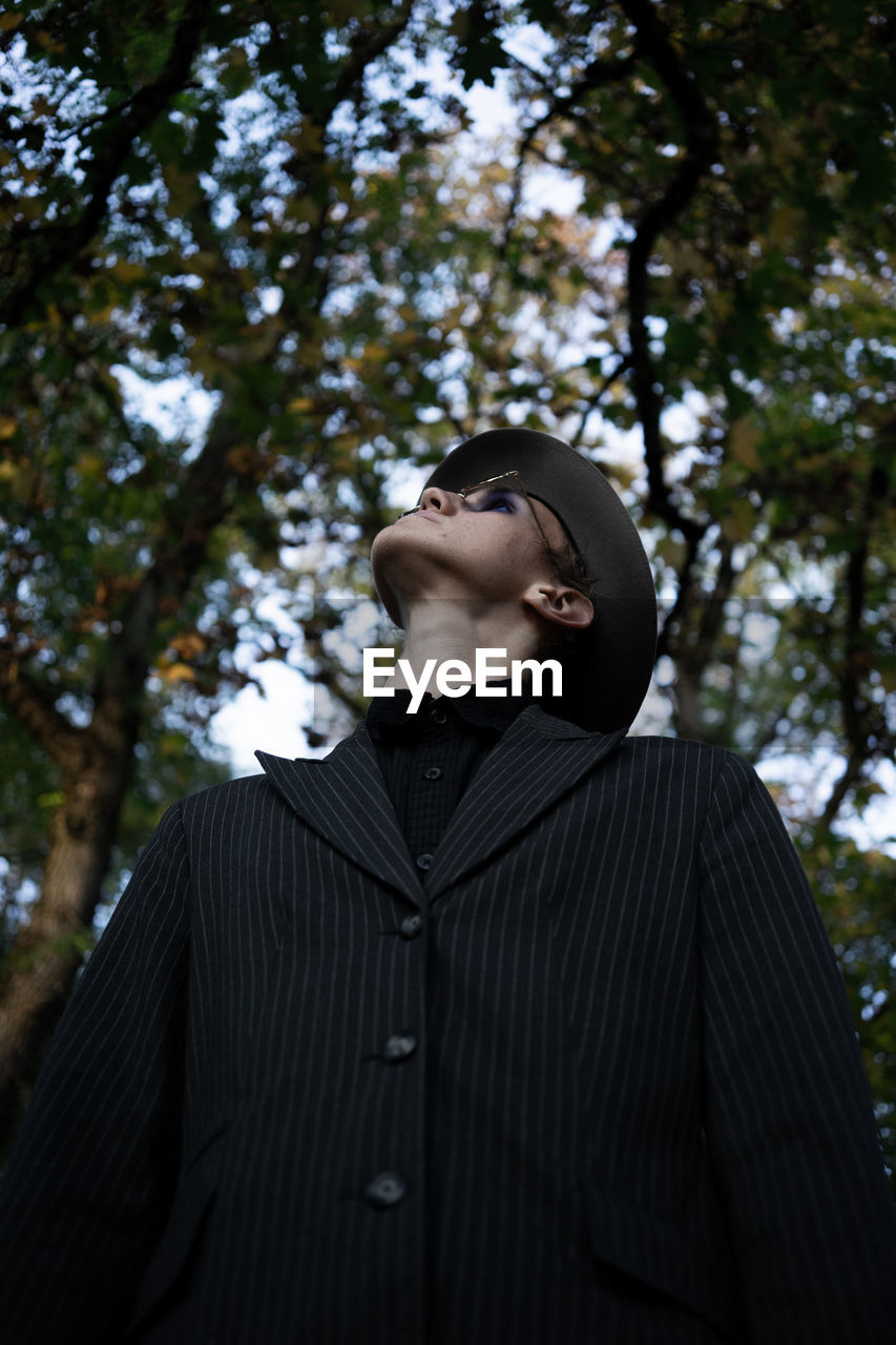 Low angle view of man looking up while standing against trees