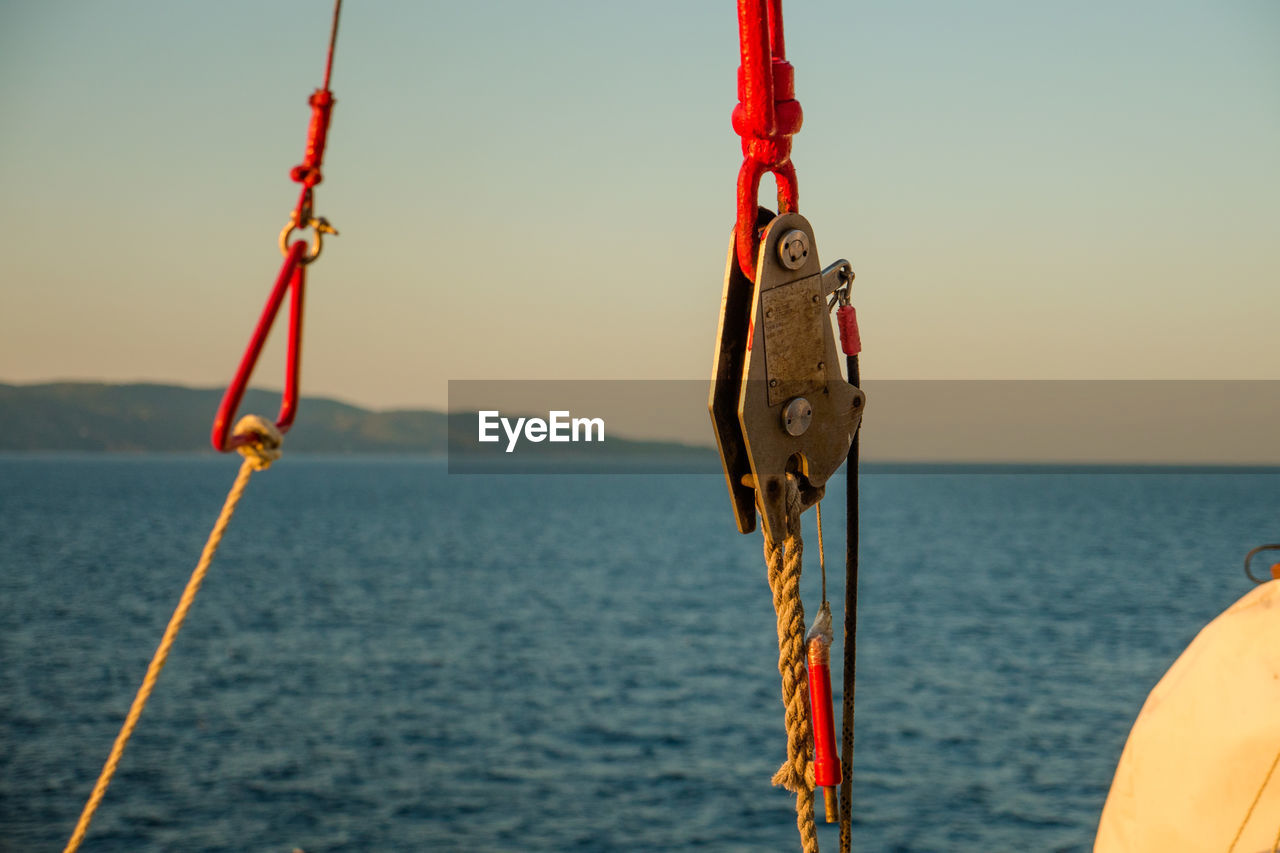 CLOSE-UP OF RED SWING HANGING AGAINST SEA