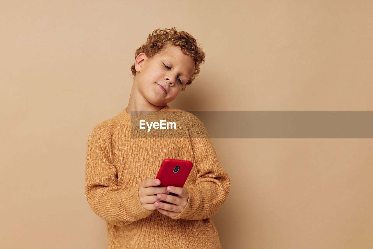 Boy using mobile phone against beige background