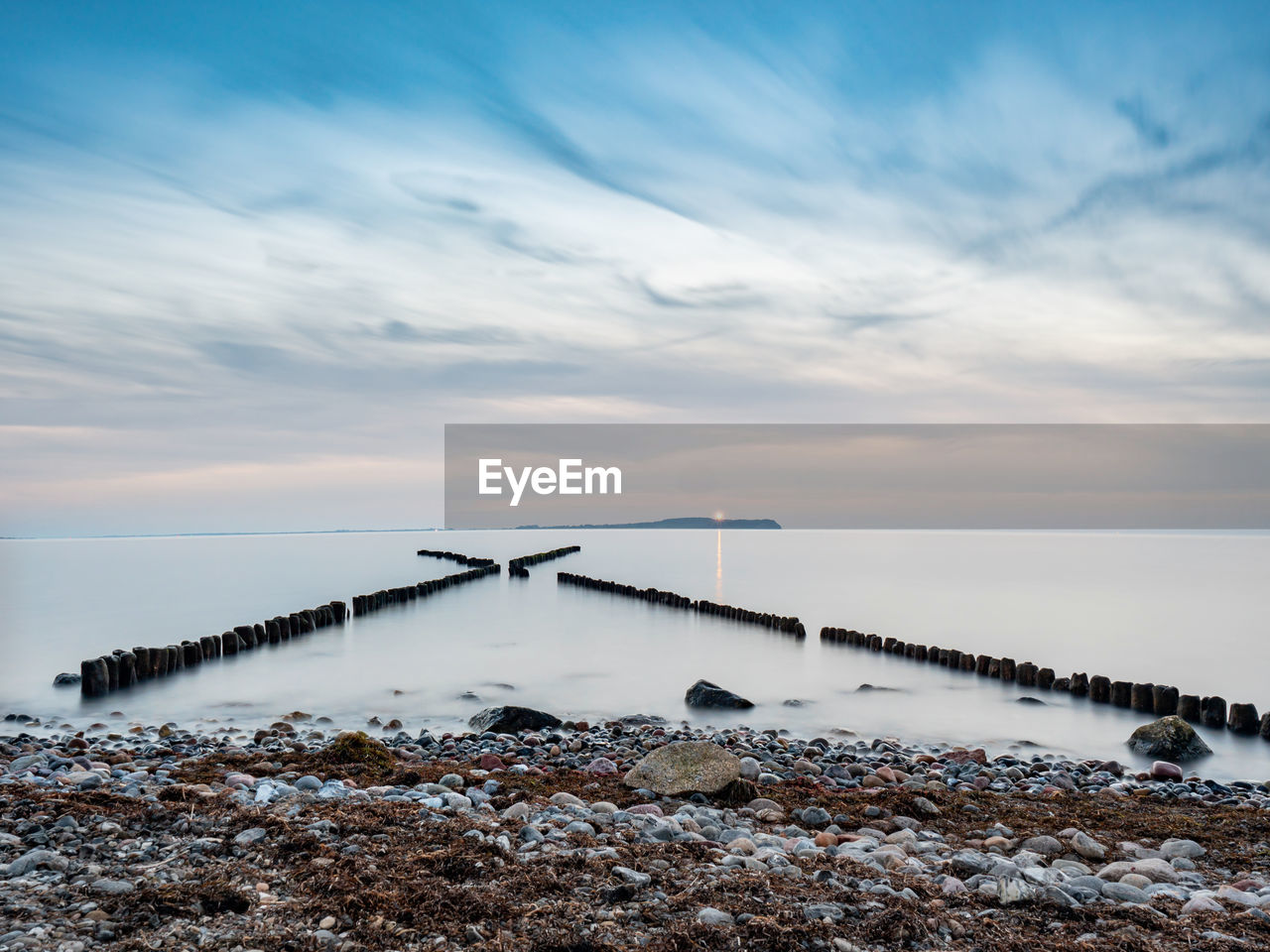 Crossed breakwater. ruegen island. morning mood at shore. hiddensee island with shinning lighthouse