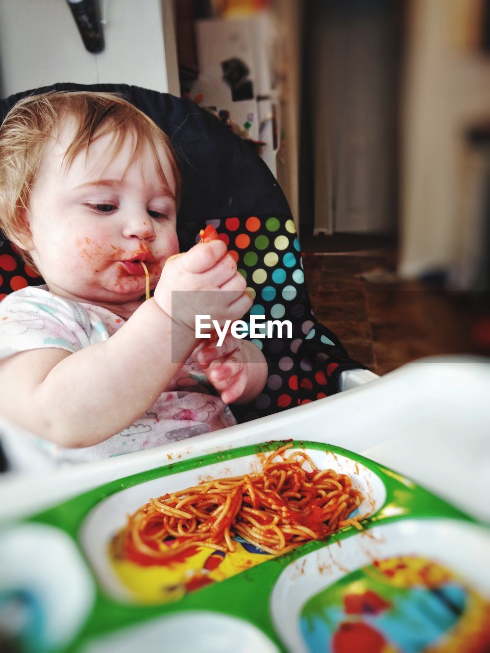 Cute baby girl eating spaghetti at home