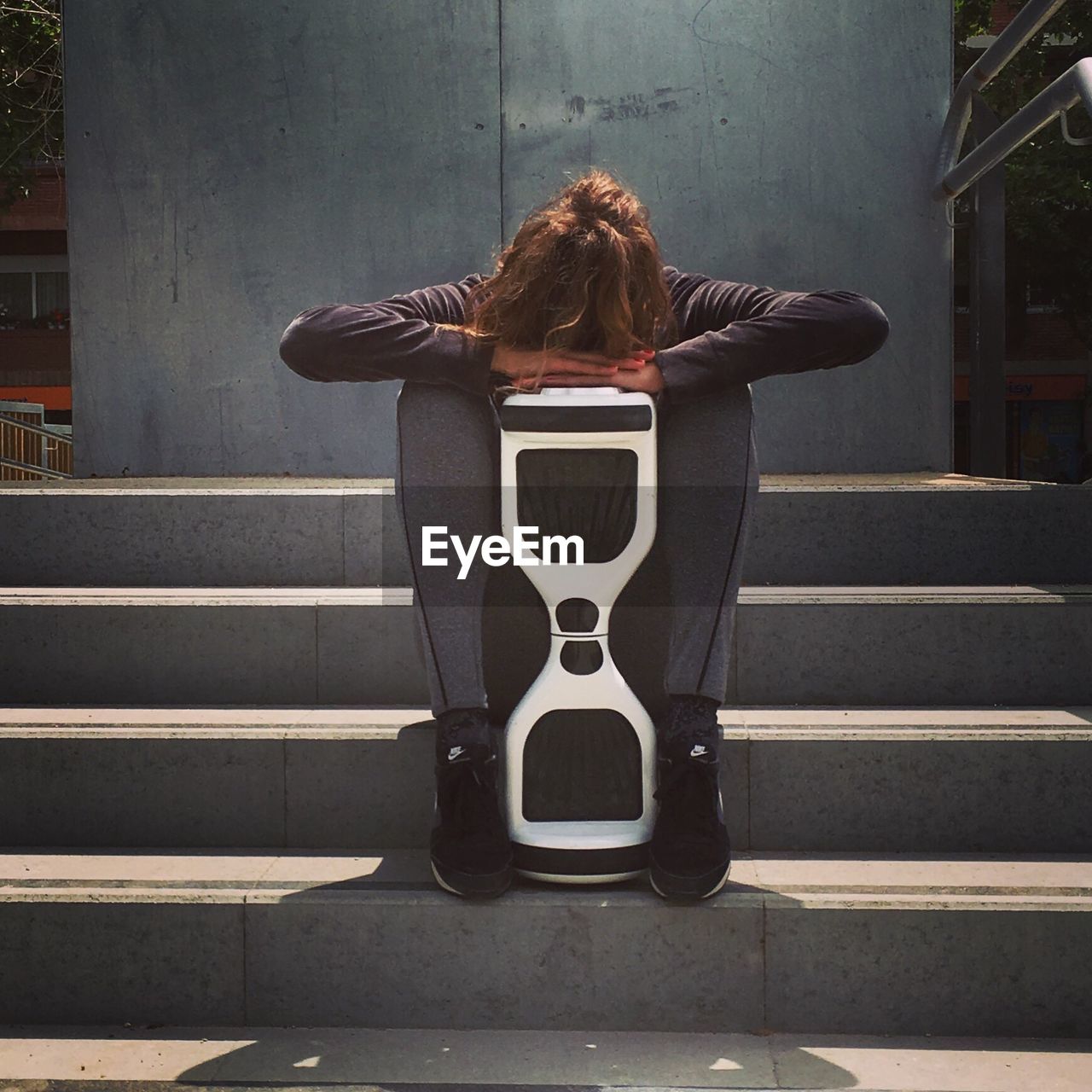 Full length of woman sitting with hoverboard on steps