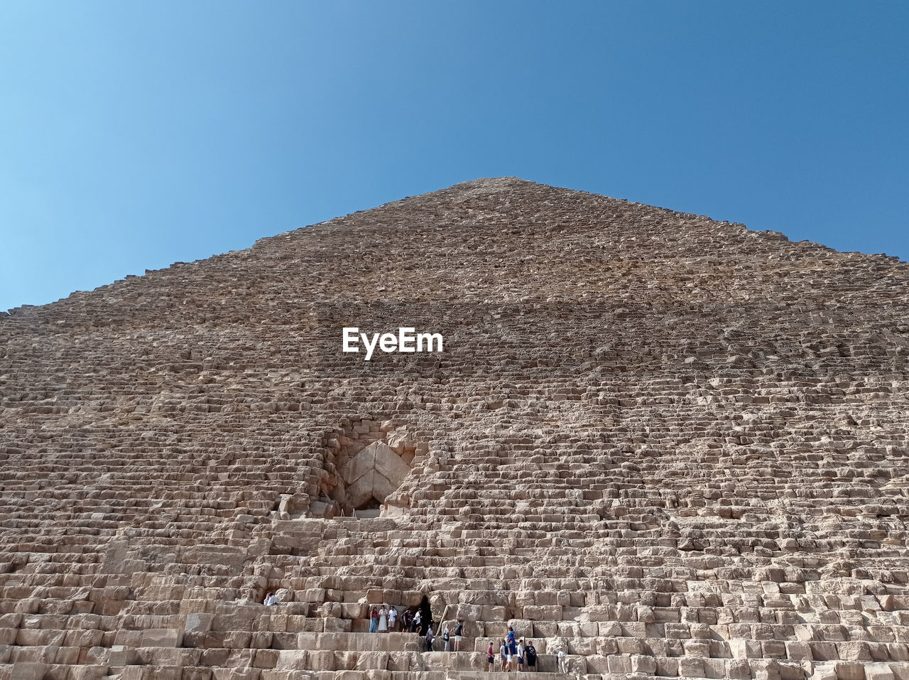 monument, architecture, pyramid, history, archaeological site, the past, sky, ancient, travel destinations, travel, built structure, ancient history, nature, blue, tourism, clear sky, ancient civilization, day, old ruin, building exterior, archaeology, outdoors, group of people, sunny, desert, city, historic site, land, tourist, landscape, stone material, environment, sunlight