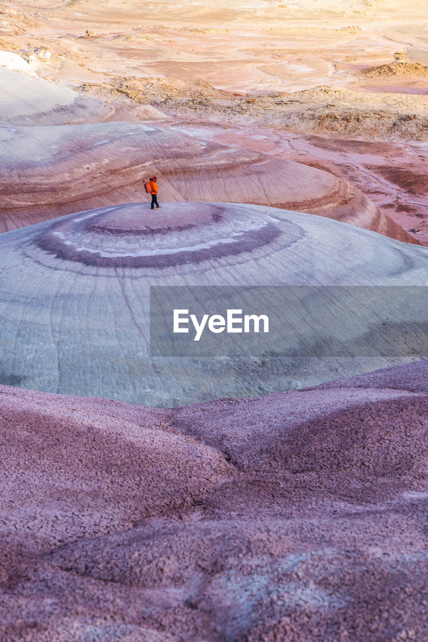 High angle of traveler in outerwear with backpack standing on top of smooth stone formation while exploring bentonite hills in utah, usa