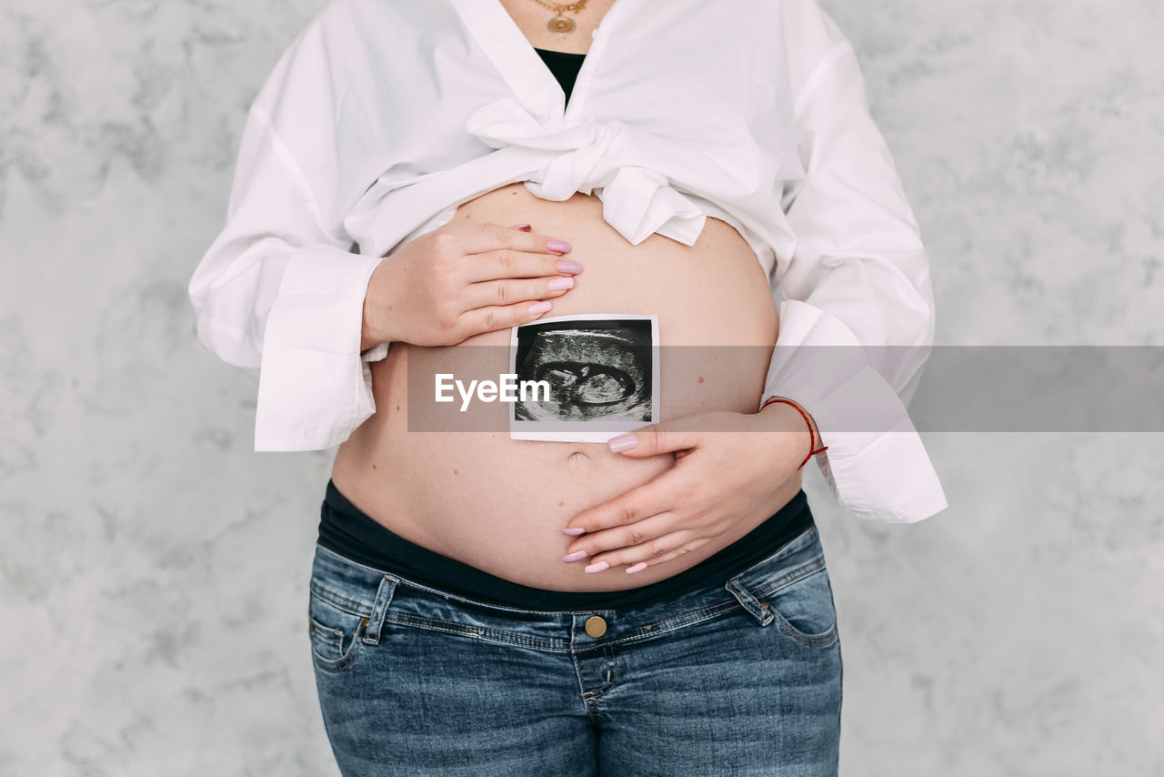 midsection of woman holding paper currency while standing against wall