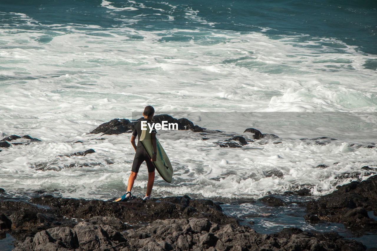 FULL LENGTH REAR VIEW OF MAN STANDING ON ROCK