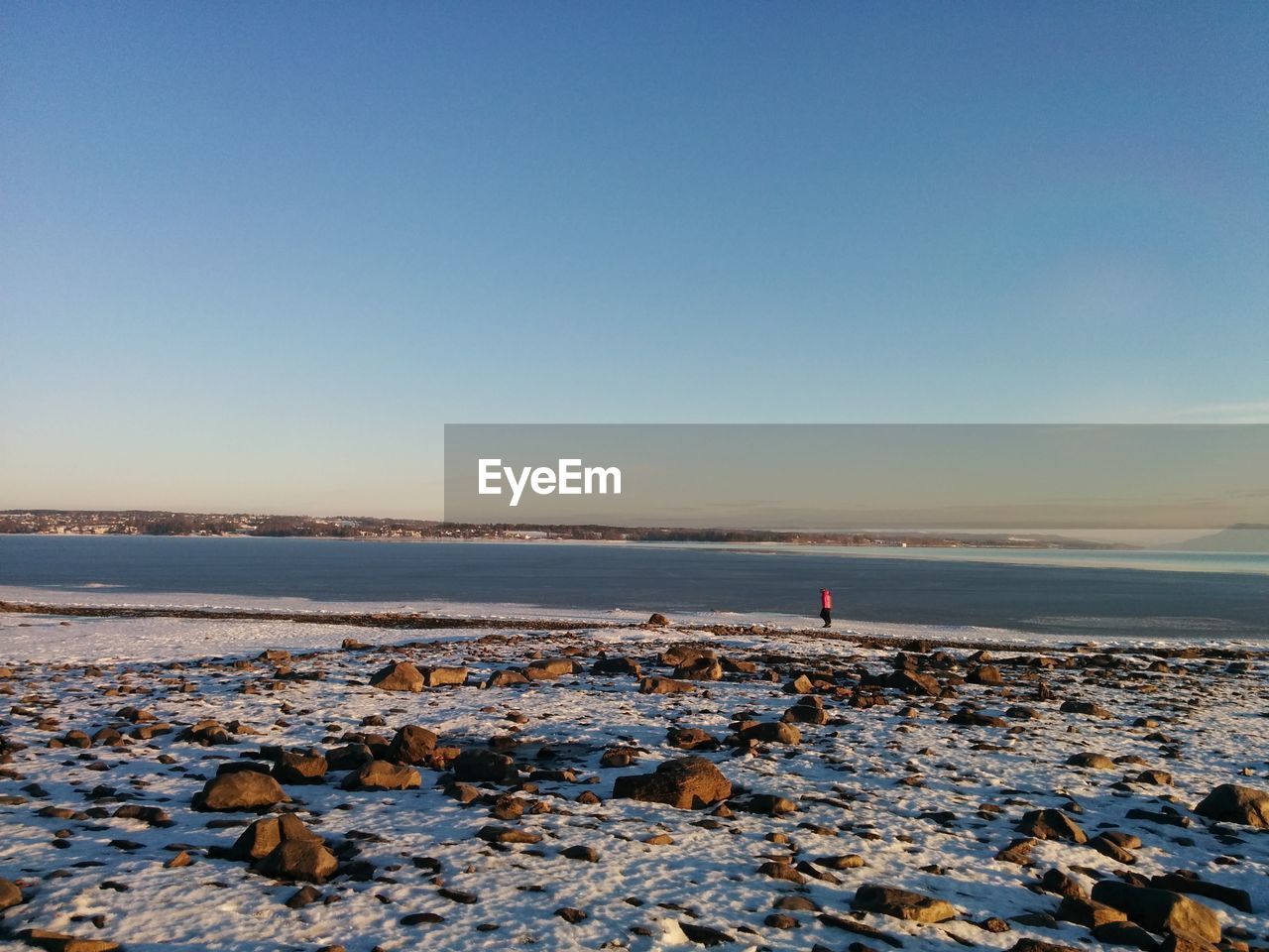 Mid distance view of person standing at frozen riverbank against sky