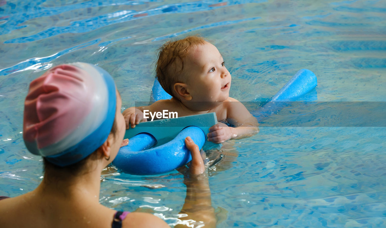 Early age swimming in pool. baby boy trained to swim in water. happy child with trainer woman in