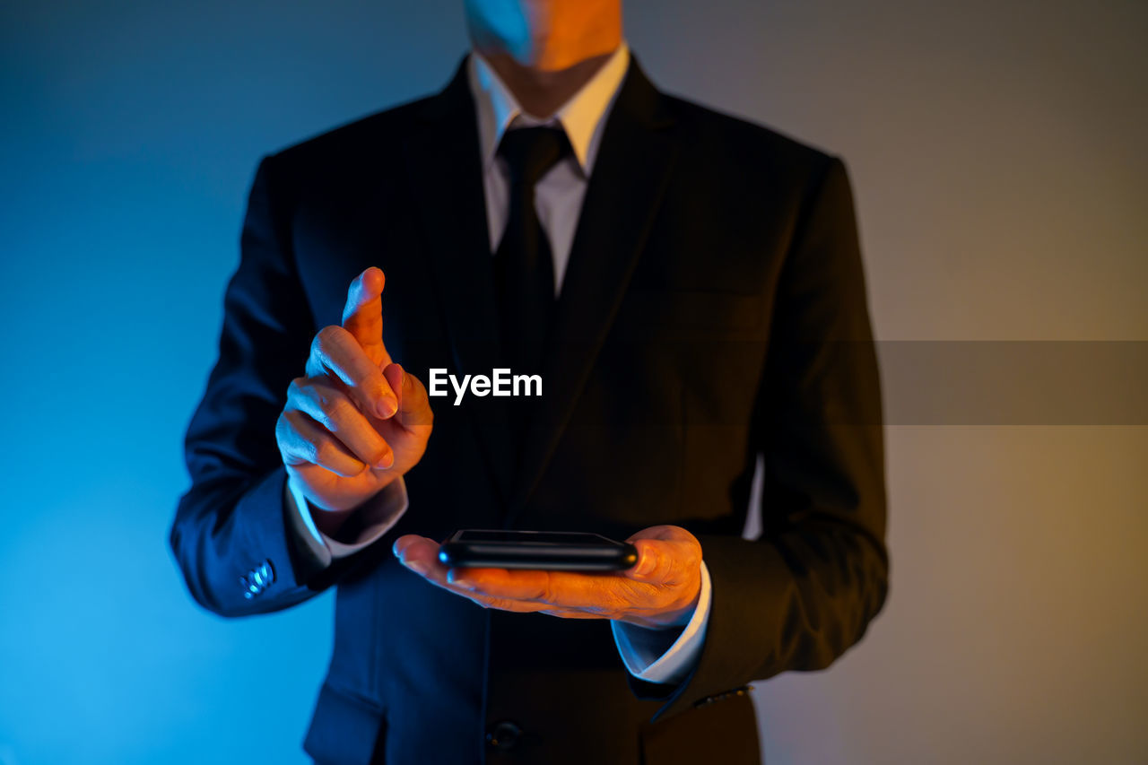 MIDSECTION OF MAN HOLDING CAMERA WHILE STANDING ON LAPTOP