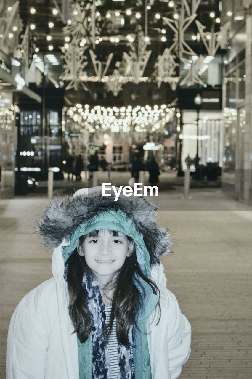 Portrait of smiling girl in warm clothing standing on street at night