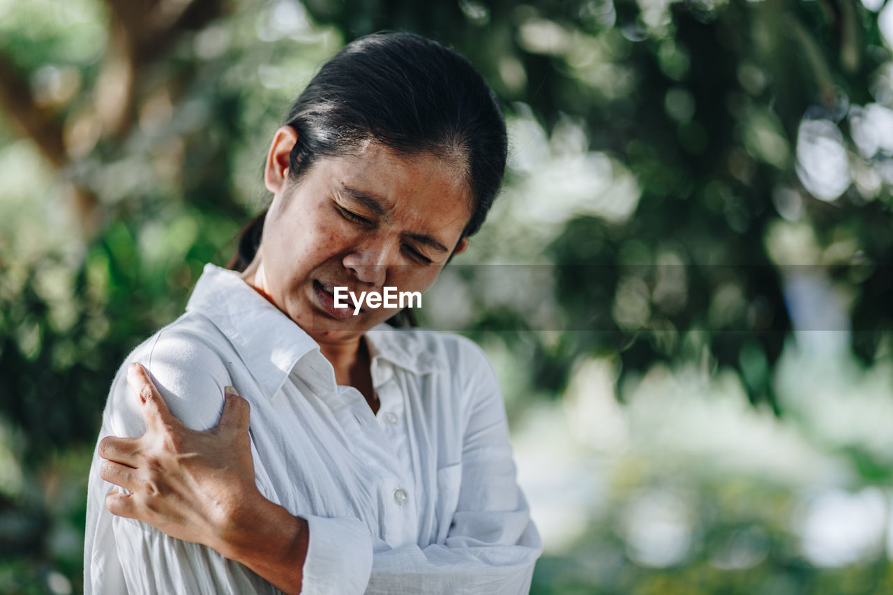 Woman with arm pain standing against trees