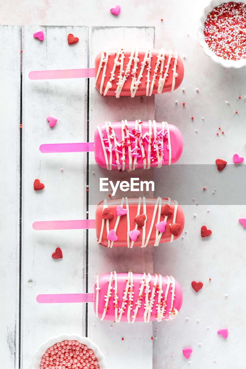 Valentine's day cakesicles on a rustic wooden board with sprinkles all around.