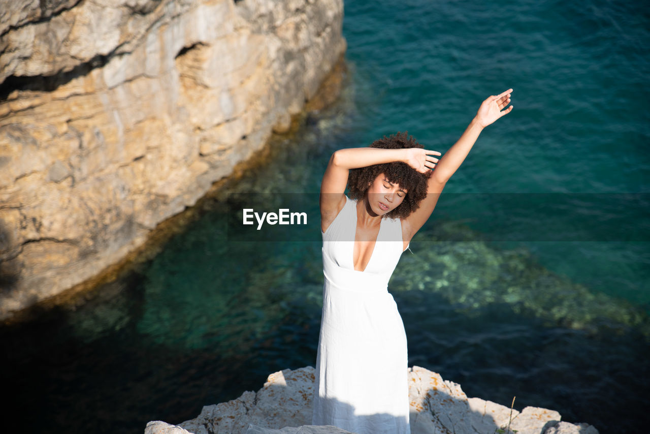 High angle view of woman with arms raised standing on cliff against sea