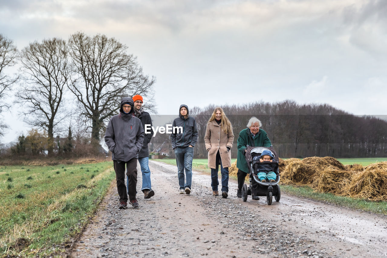 Family walking on dirt road against sky
