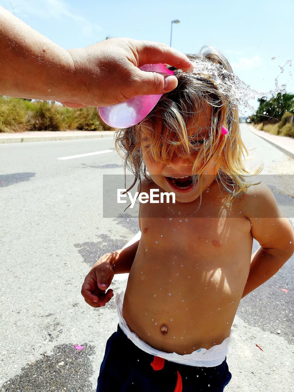 Cropped hand of bursting water bomb on girl head