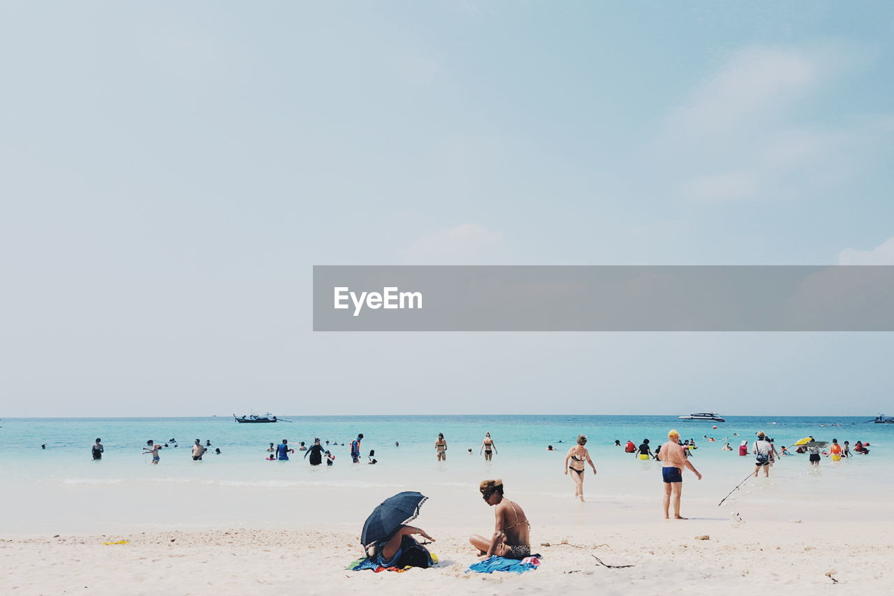 People at beach against cloudy sky on sunny day