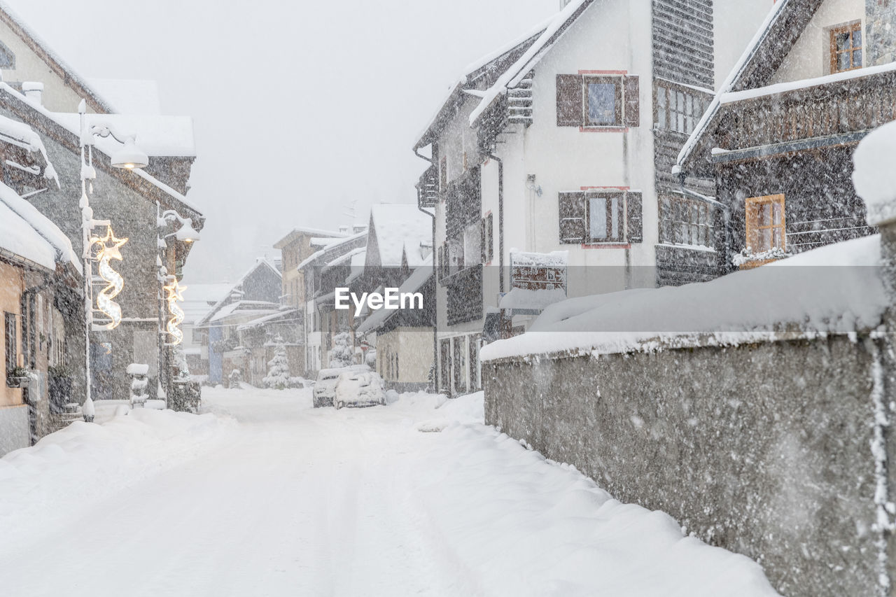 SNOW COVERED STREET BY HOUSES IN CITY DURING WINTER