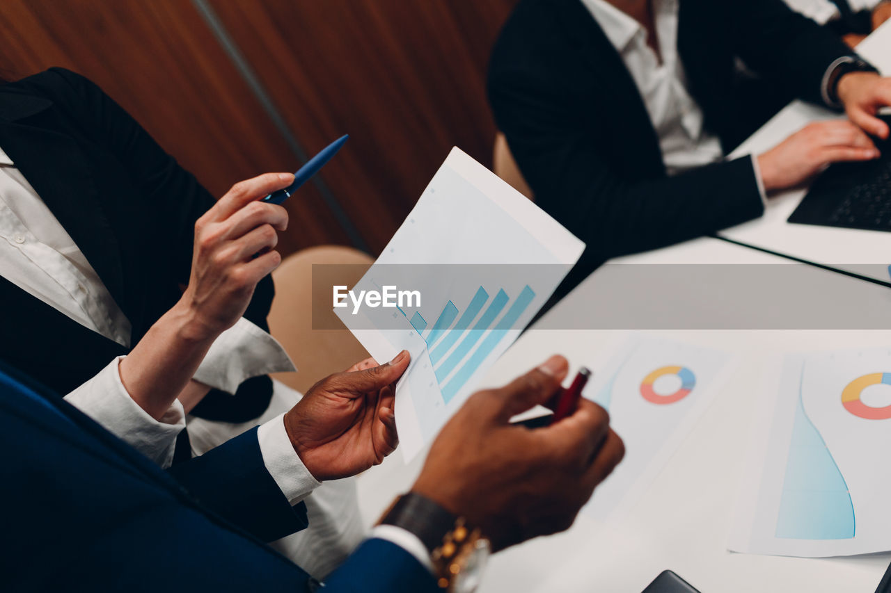 HIGH ANGLE VIEW OF PEOPLE WORKING ON TABLE IN OFFICE