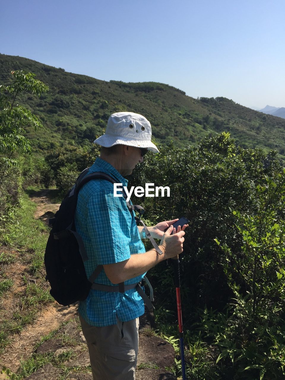 Man using phone while hiking on mountains against clear sky