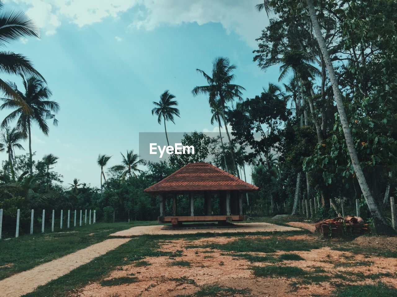 Gazebo by palm trees on field against sky