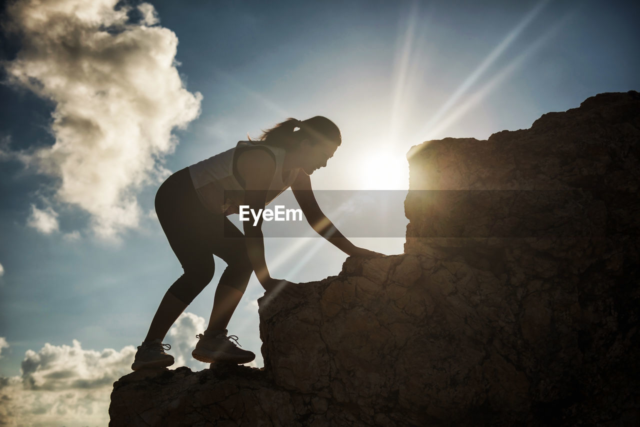 Low angle view of woman climbing on rock against sky