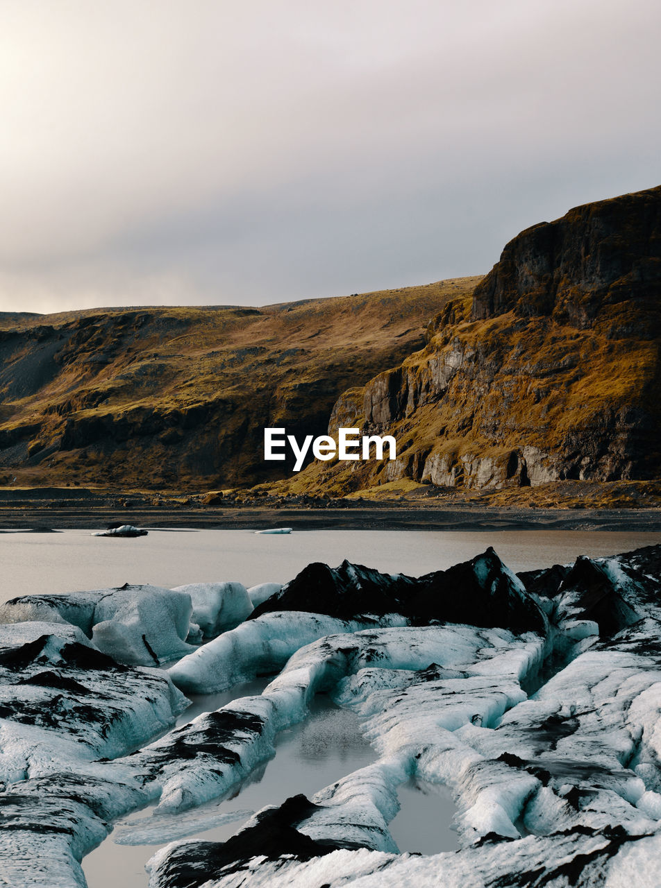 Scenic view of sea by mountains against sky during winter