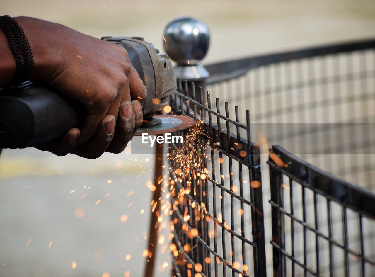 Cropped hands of worker cutting fence with electric saw