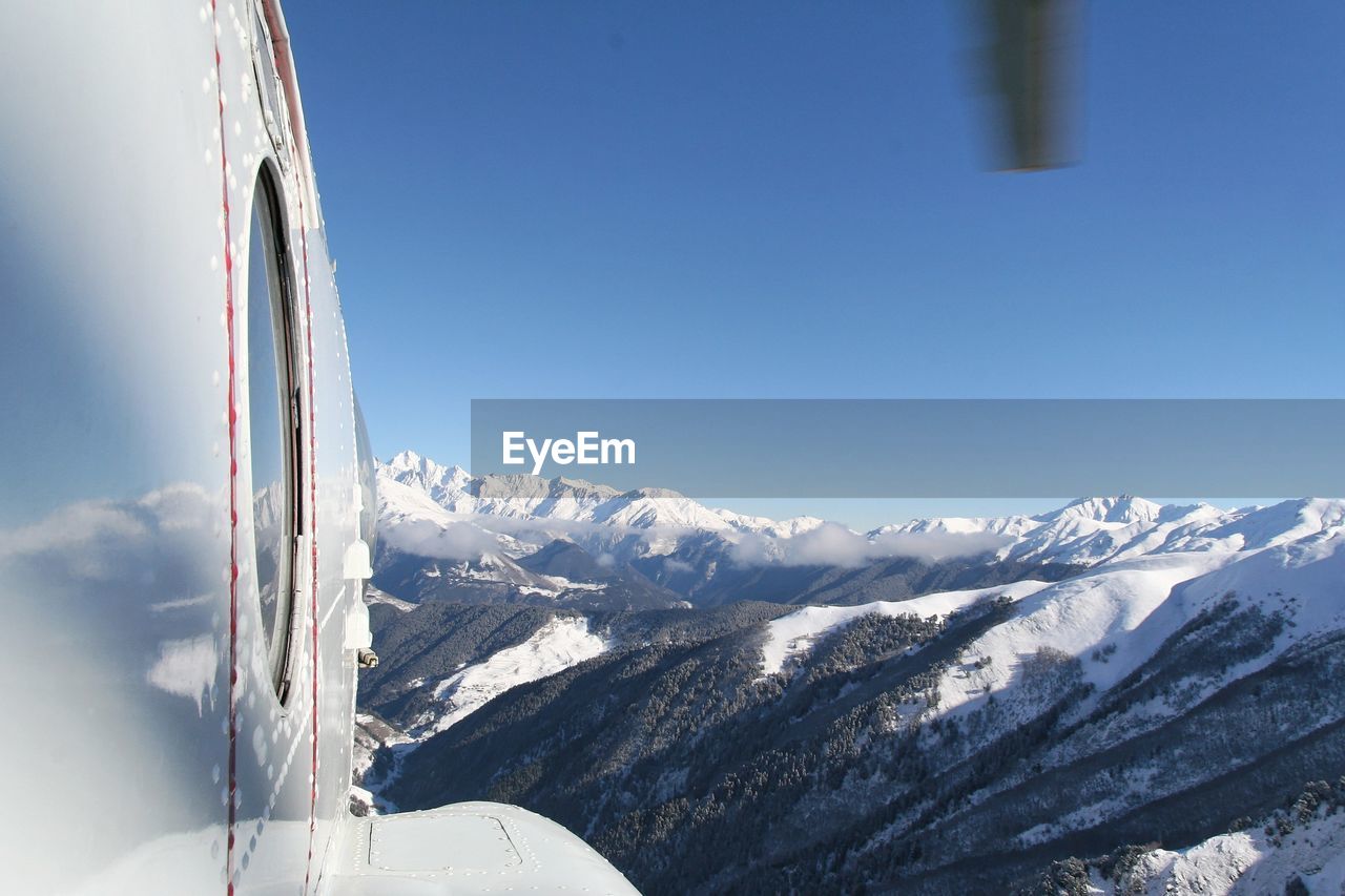 Cropped image of airplane flying over snowcapped mountains against blue sky