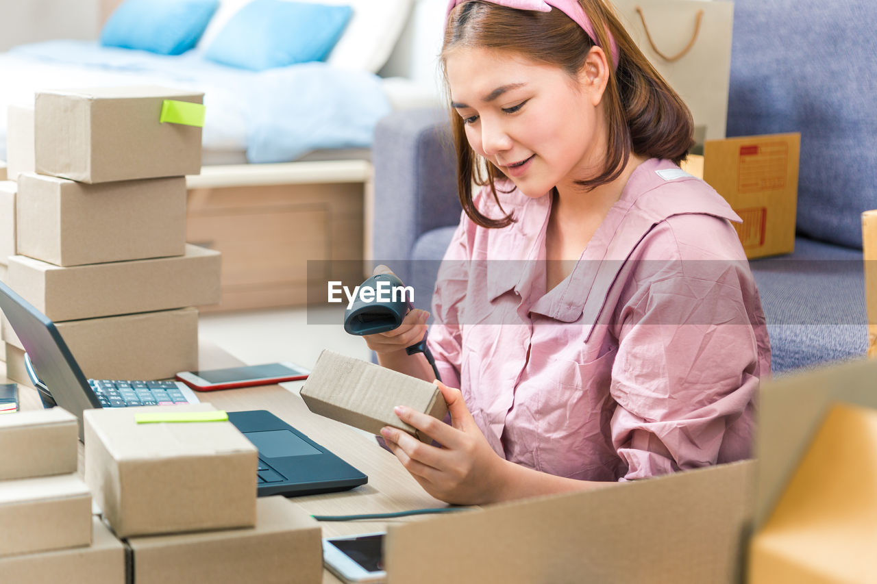 Woman scanning cardboard box with bar code reader at home