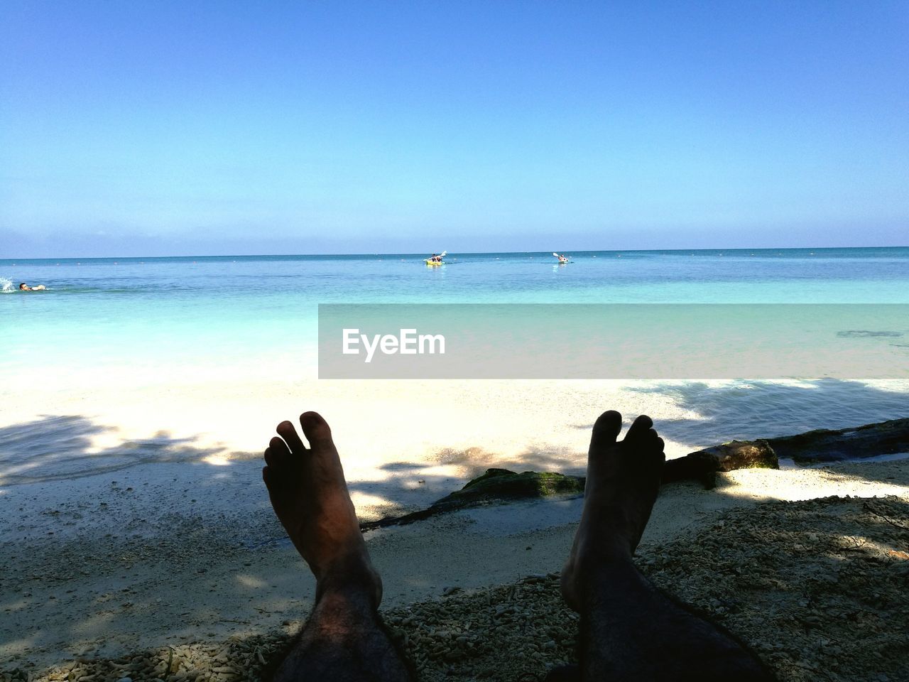 Low section of man on beach against clear blue sky