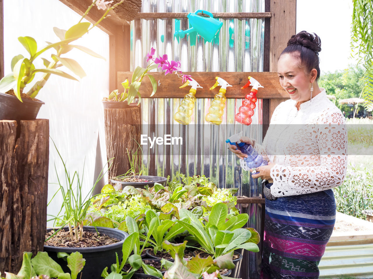 WOMAN HOLDING FLOWER POT STANDING BY POTTED PLANT