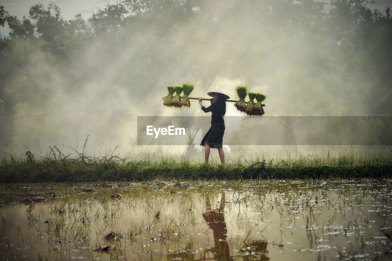 Side view of farmer carrying crops while walking on field