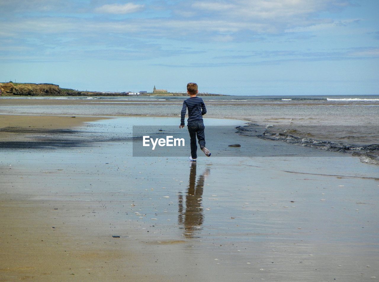 Rear view of boy running on shore at beach