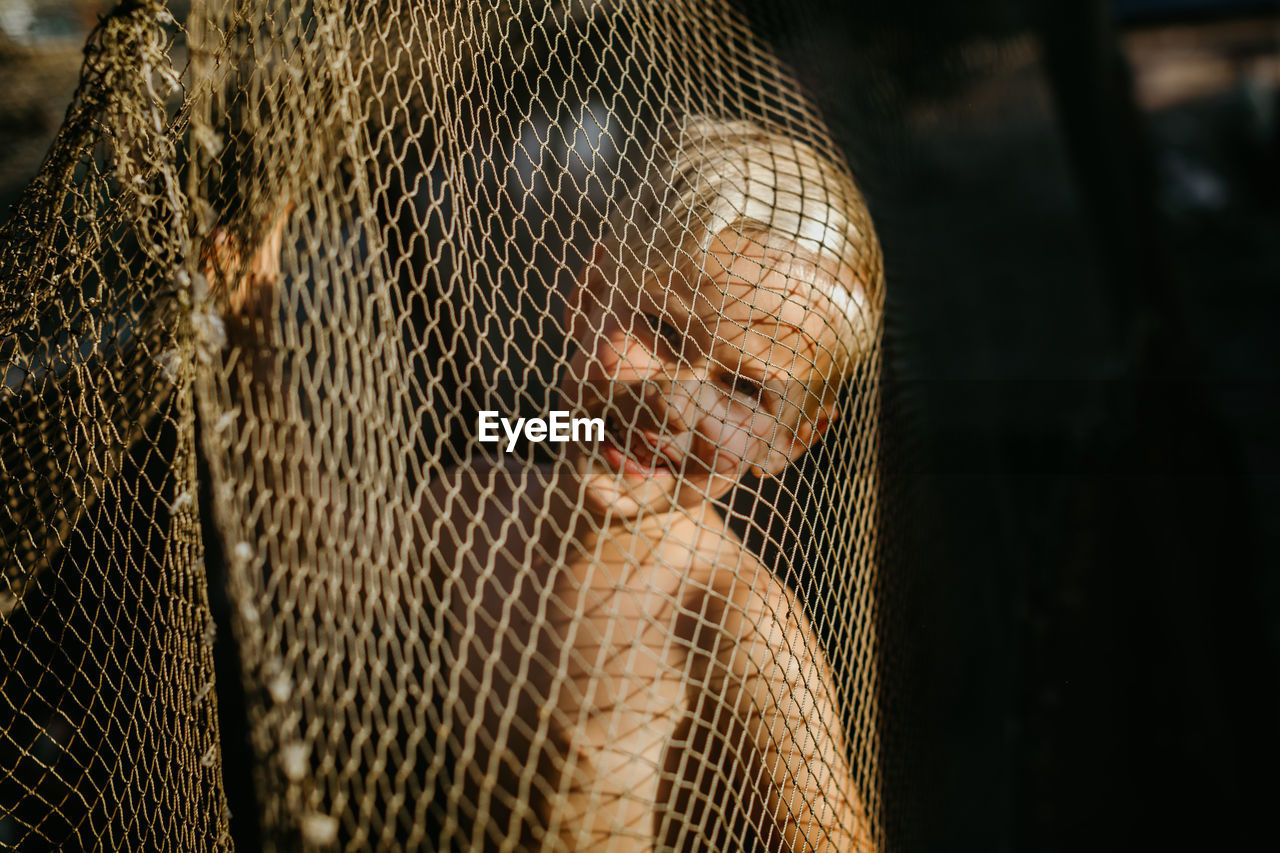 Close-up portrait of cute boy seen through net