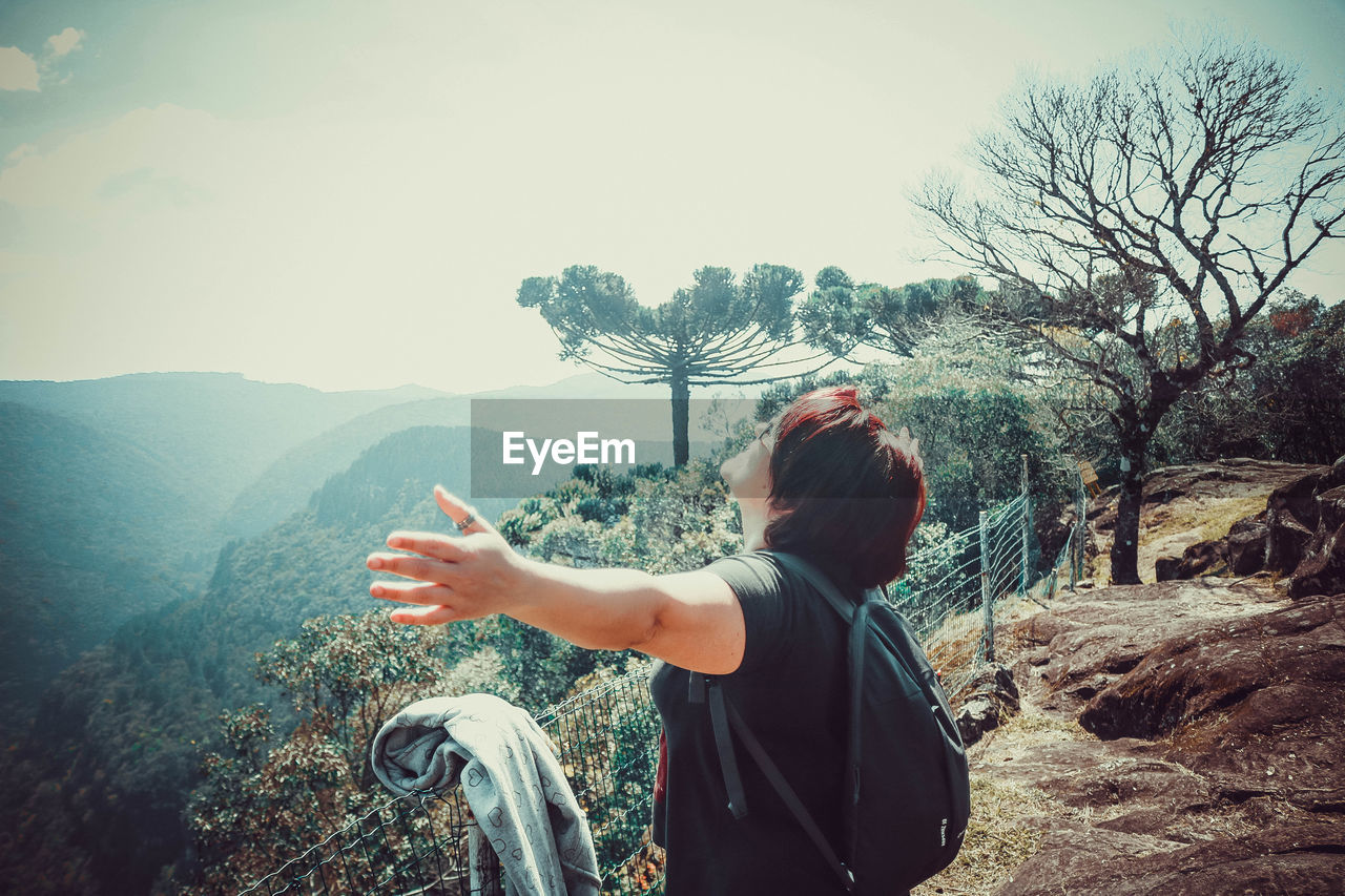 Side view of woman with arms outstretched standing on mountain against sky