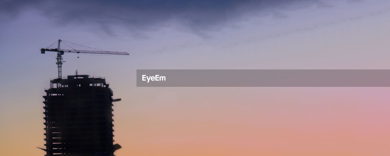 LOW ANGLE VIEW OF CRANE BY BUILDING AGAINST SKY