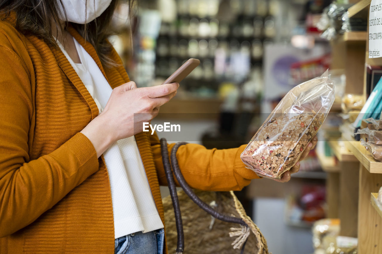 Young woman photographing organic food package in grocery store