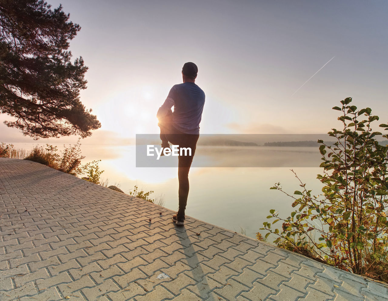 Runner stretching leg in front of river. athletic sport man stretching leg muscles before run 