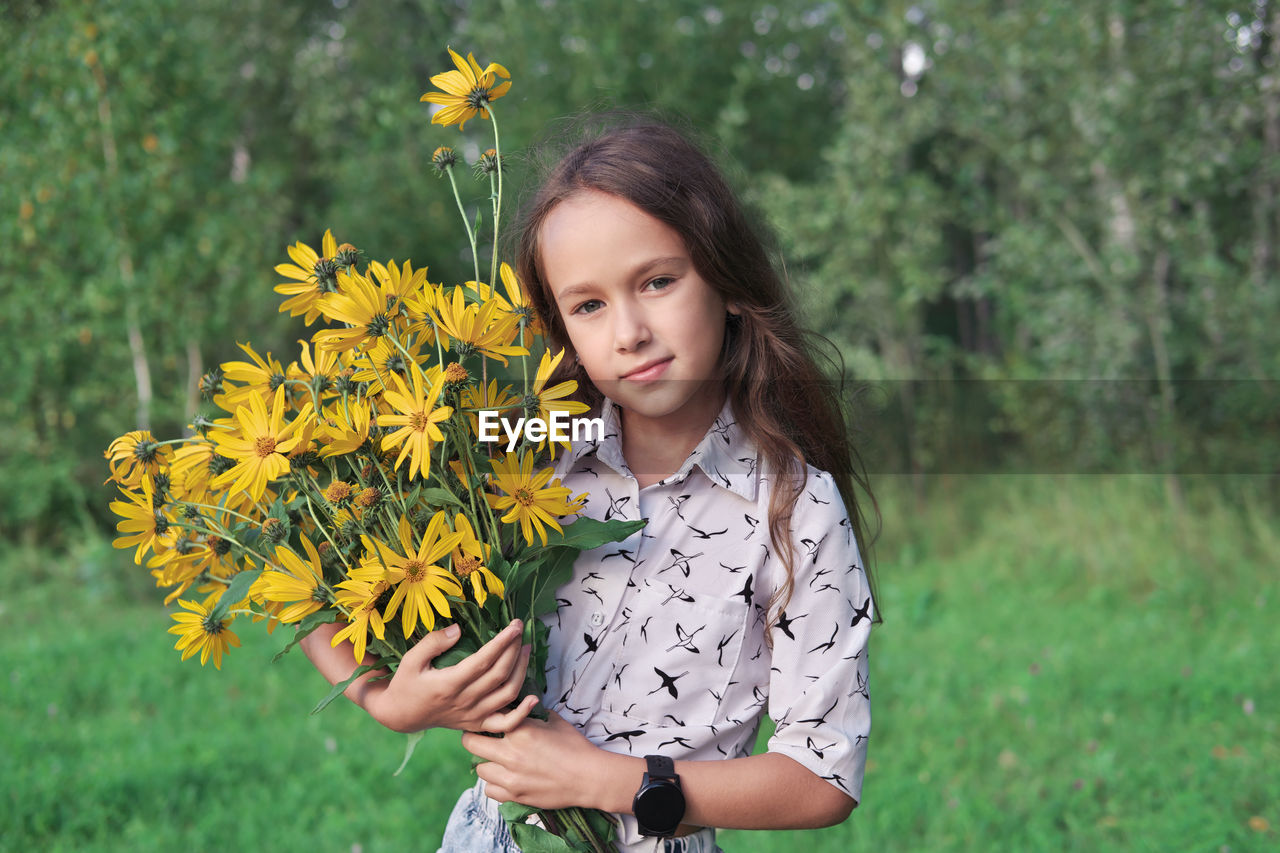 Little girl holding a bouquet of topinambur flowers. bright yellow flowers. summer country concept. 