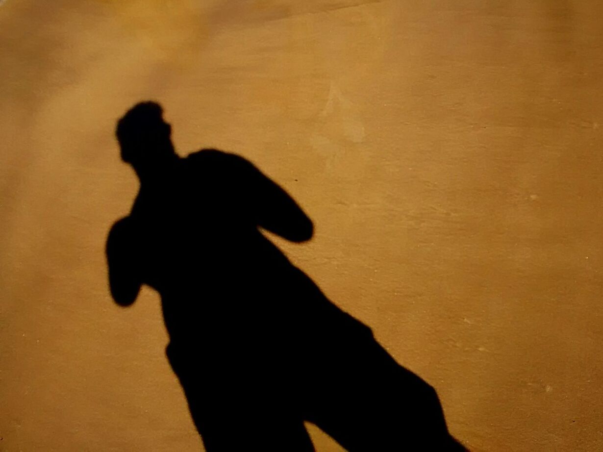 SILHOUETTE MAN STANDING AGAINST ORANGE SHADOW ON WALL