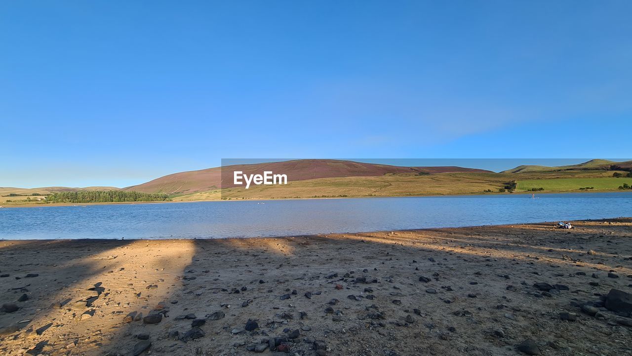 sky, water, sea, land, scenics - nature, shore, coast, landscape, mountain, beauty in nature, nature, sand, body of water, environment, horizon, blue, tranquility, beach, ocean, clear sky, no people, natural environment, tranquil scene, travel destinations, day, non-urban scene, travel, outdoors, desert, reservoir, sunny, tourism, reflection, bay, copy space, mountain range, animal wildlife, remote