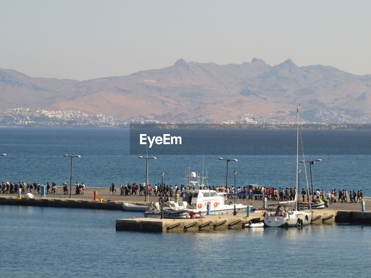 People on pier at port on sea against mountains