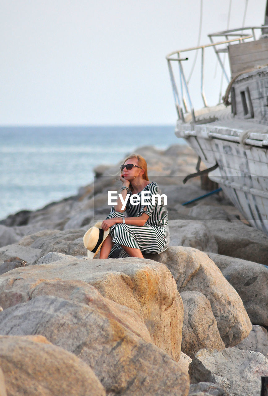 Woman sitting on rock at sea against sky