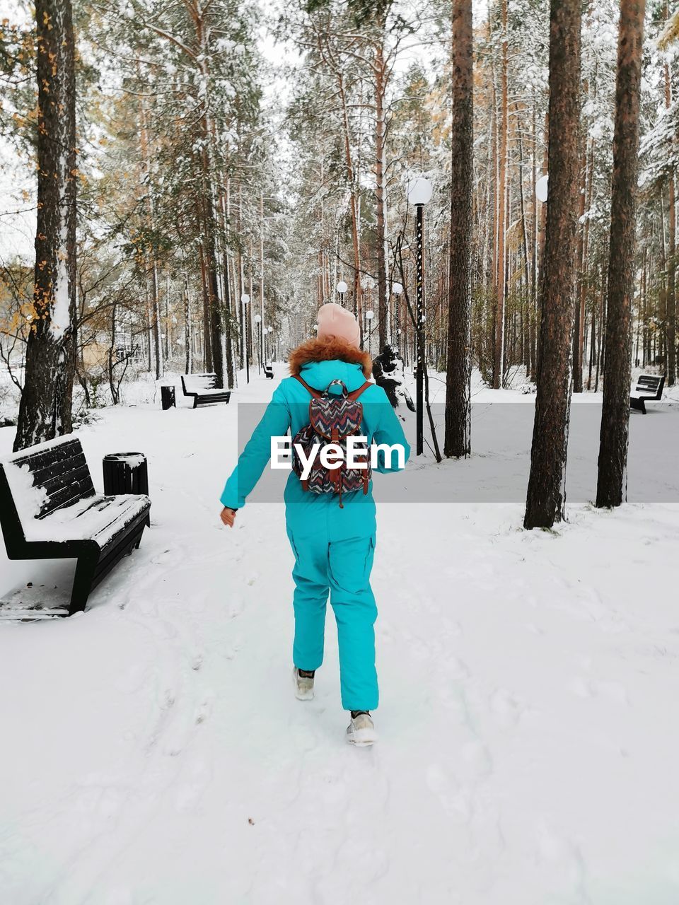 A girl in a sports jumpsuit walks in the park in winter.