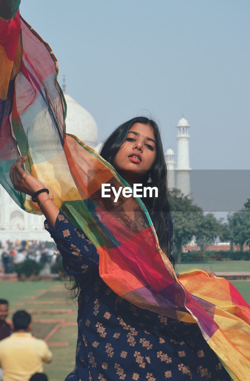 Portrait of smiling young woman standing against taj mahal